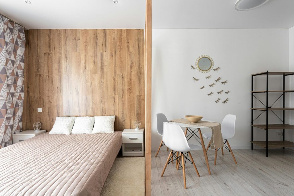 Bed with cushions against table and chairs on floor at home with empty shelves and decorative dragonflies on wall